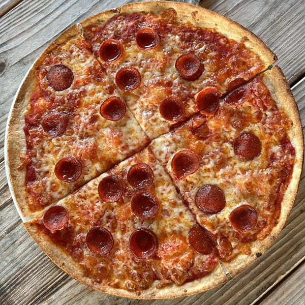 A whole pepperoni pizza, cut into six slices, rests on a rustic wooden table.