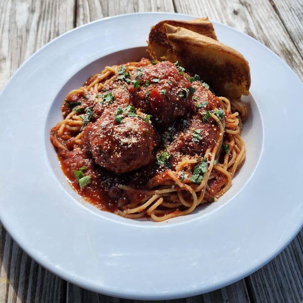 Spaghetti and meatballs with tomato sauce, parmesan, and basil, served with garlic bread.