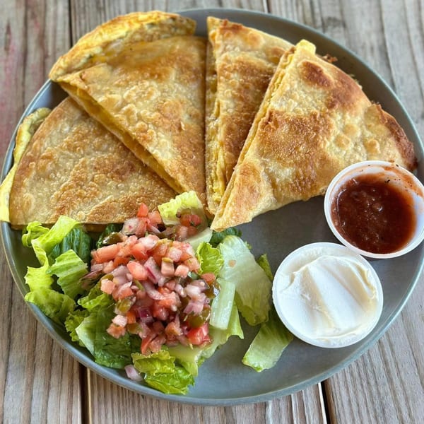 Golden-brown quesadilla wedges with a side salad, salsa, and sour cream on a gray plate.
