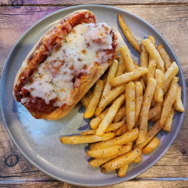 Meatball sub with melted cheese and marinara sauce, served with a side of seasoned fries.