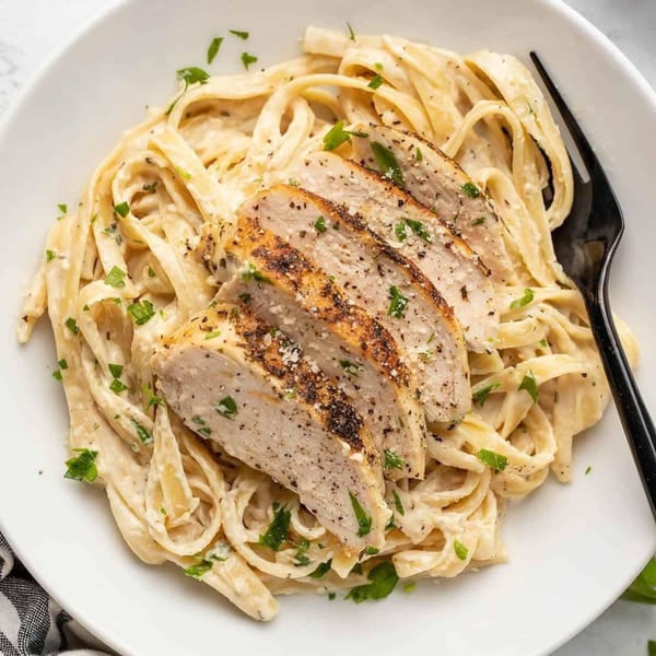 Creamy fettuccine alfredo with sliced grilled chicken, sprinkled with parsley and black pepper.