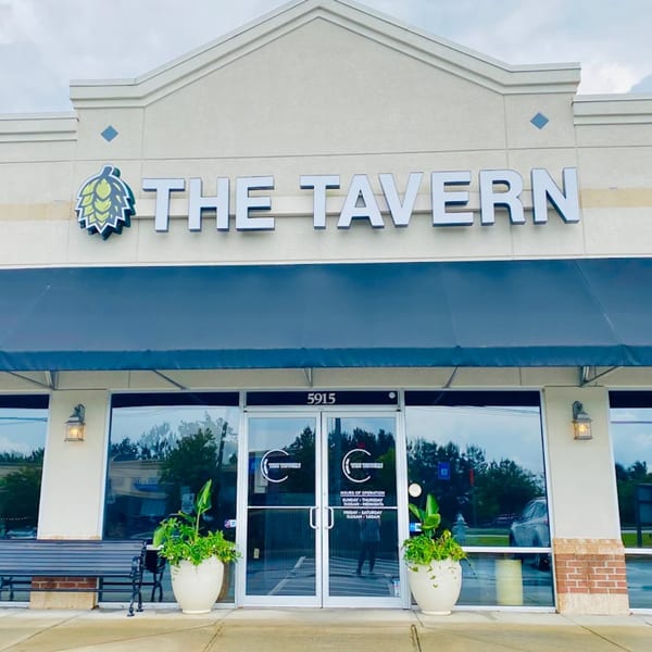 The Tavern at Sugar Hill storefront with a blue awning, glass doors, and a hop logo.