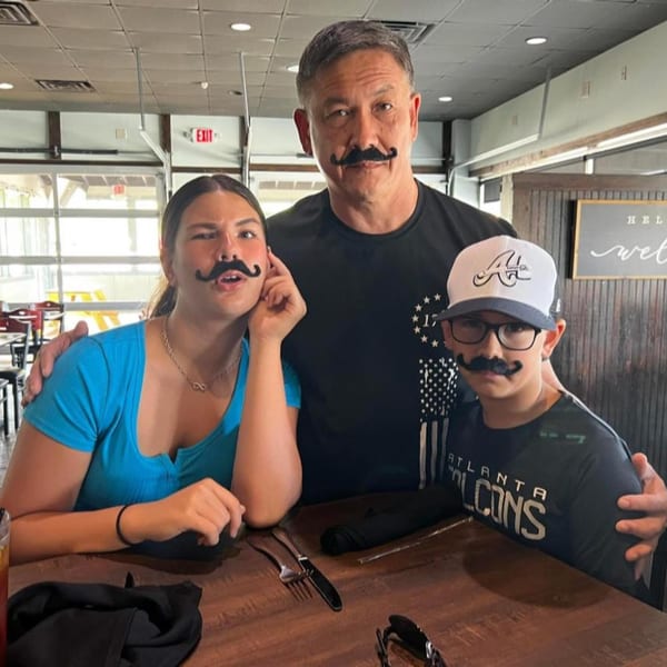 Father and two children wearing fake mustaches, smiling at a table in The Tavern at Sugar Hill.