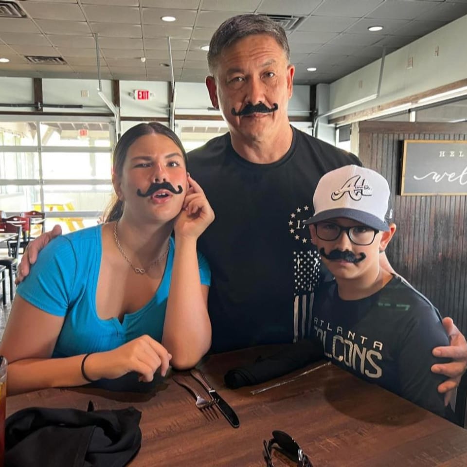 Father and two children wearing fake mustaches, smiling at a table in The Tavern at Sugar Hill.