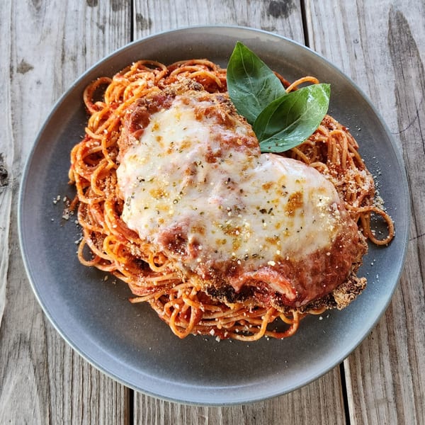 Chicken Parmesan with spaghetti, red sauce, melted cheese, and basil on a gray plate.